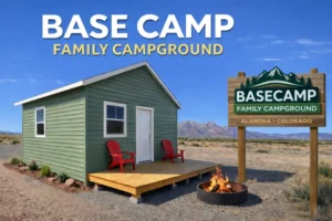 A small green cabin with red chairs, a fire pit, and a BASE CAMP sign in a dry landscape with mountains in the background.