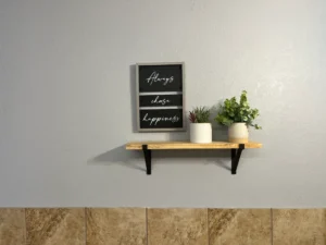Wooden wall shelf with two potted plants and a framed sign that reads "Always chase happiness" on a gray wall.
