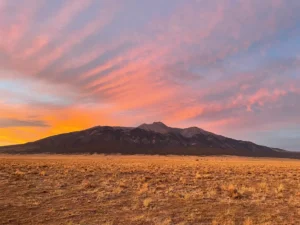 A grassy plain with a mountain range in the distance under a colorful pink and orange sunset sky.