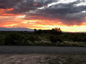 Sunset over a grassy landscape with mountains in the distance and dramatic clouds in the sky.