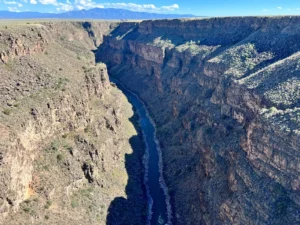 A deep canyon with steep rocky cliffs and a river flowing through the bottom, under a clear blue sky.
